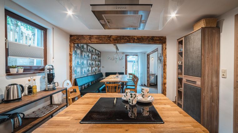Een moderne keuken met een houten werktafel en kookplaat in het midden. De ruimte heeft lichte muren en gezellige zitgelegenheden met een uitnodigende sfeer.