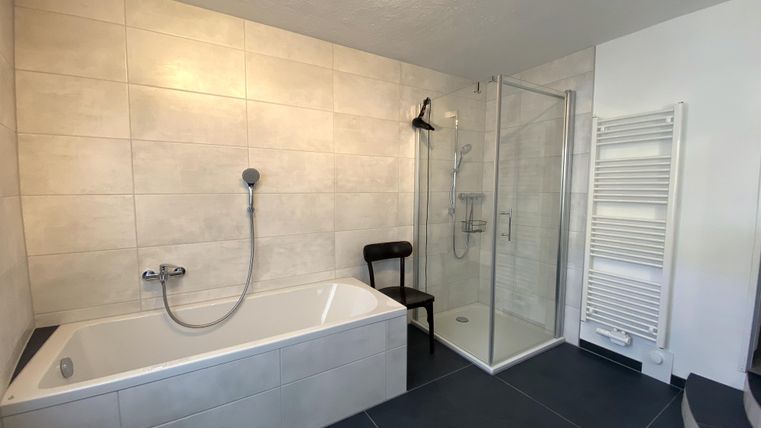 Een moderne badkamer met een bad en een aparte douche. De muren zijn licht betegeld en er is een handdoekradiator.