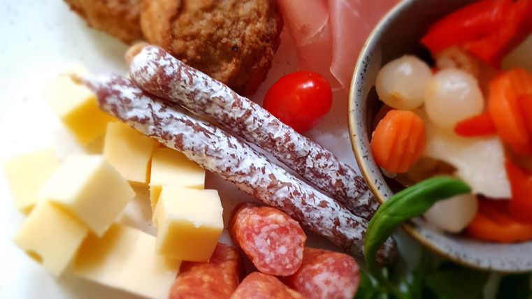 A plate with various delicacies, including sausage, cheese, ham, and vegetables. The arrangement is appealing and colorful.