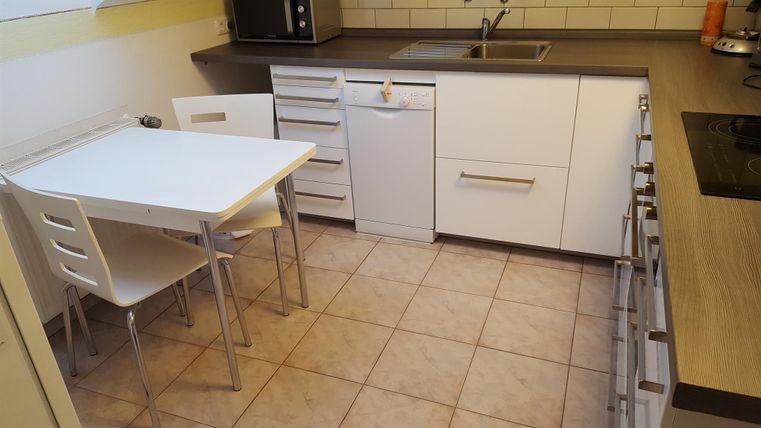 Een moderne keuken met witte kasten en een kleine eethoek. De vloer is betegeld en het werkblad is van hout.