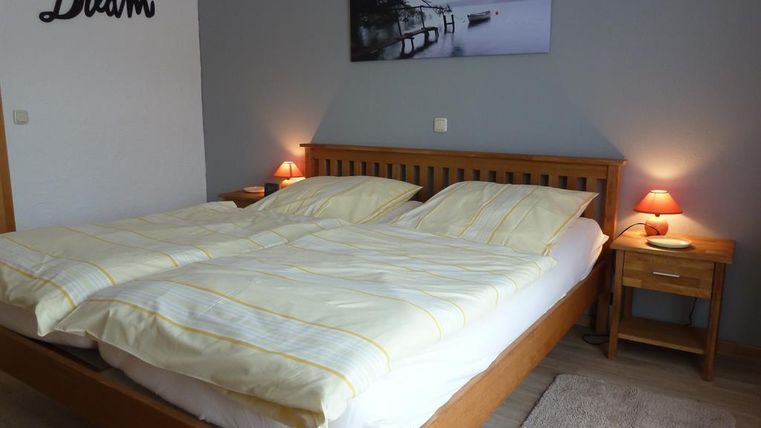 A modern bedroom with a large double bed and soft lighting. A calming landscape painting hangs on the wall.