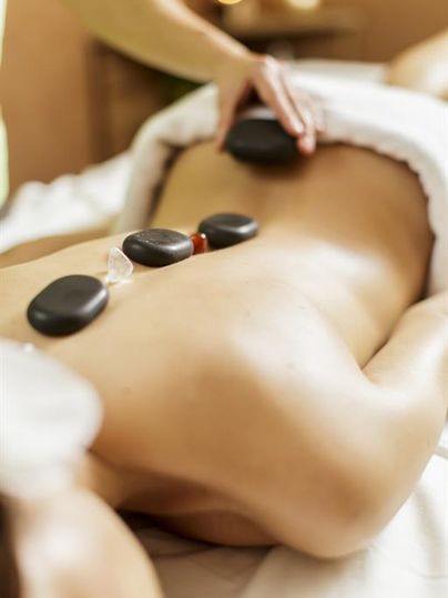 Eine entspannende Massage mit heißen Steinen auf dem Rücken. Sanfte Hände sorgen für Wohlbefinden und Entspannung.