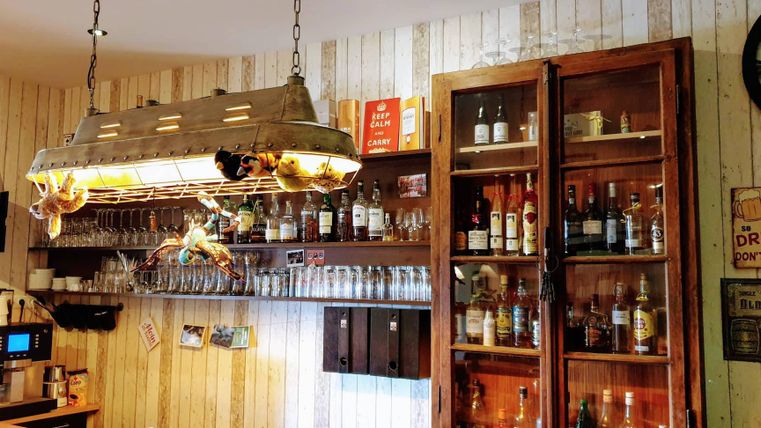 Ein gemütlicher Barbereich mit einer Holzregalwand. Die Theke ist dekoriert mit Gläsern und einer Auswahl an Spirituosen.