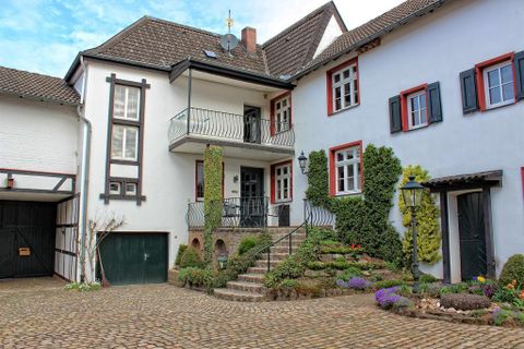 A charming house with a balcony and green plants. The courtyard is designed with flowers and a stone path.