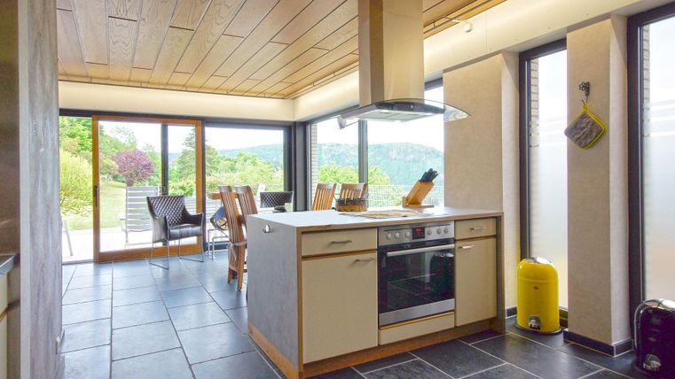 Eine moderne Küche mit Holzdecken und großen Fenstern. Der Raum hat einen stilvollen Look und viel Tageslicht.