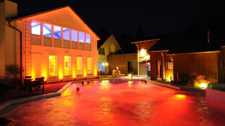 A beautiful pool at night with soft red lighting. The surrounding buildings are brightly lit, creating an inviting atmosphere.