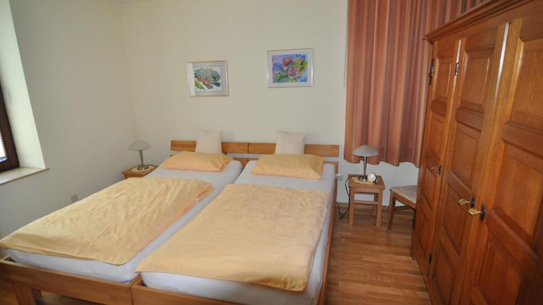 A cozy bedroom with two single beds and a wooden floor. The walls are painted light and there are some pictures as well as curtains.
