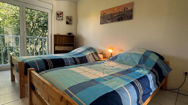 Een gezellige kamer met twee eenpersoonsbedden en kleurrijke dekbedden. Grote ramen zorgen voor veel daglicht en uitzicht op de natuur.