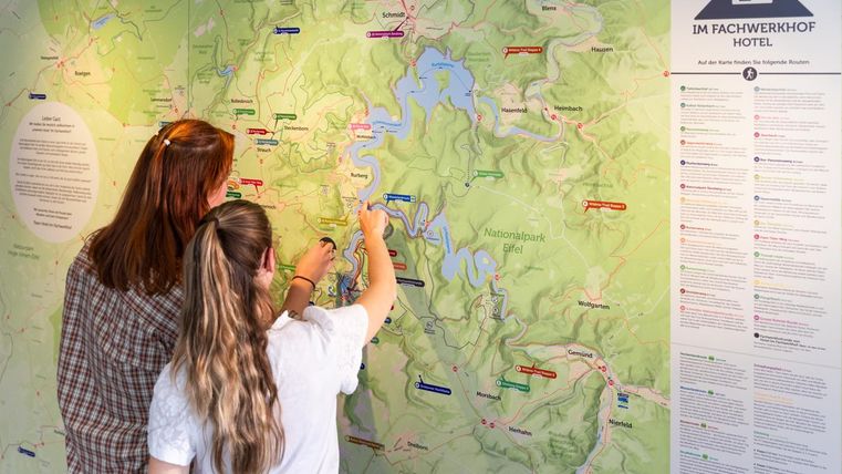 Two people are looking at a map and marking locations. In the background, information about the surroundings is visible.