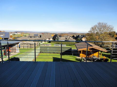 Een blik vanaf een terras op een landelijke omgeving, omgeven door huizen en groene tuinen. De lucht is helder en blauw, wat zorgt voor een aangename sfeer.