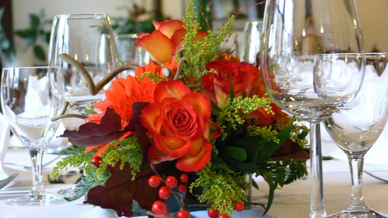 A beautifully set table with wine glasses and a floral arrangement of orange roses. The table decoration adds a festive atmosphere.