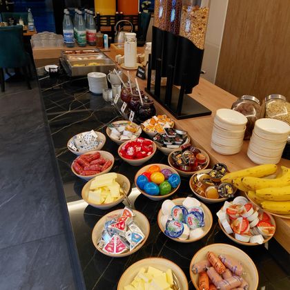 A buffet with various breakfast ingredients. There are cold cuts, cheese, fruit, and sweets as well as drinks.