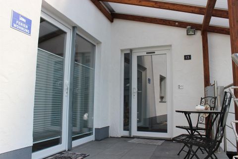 An inviting entrance area of a holiday home with a glass door and wooden canopy. A small table with two chairs is set up, perfect for a relaxed break.