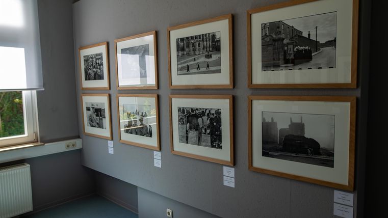 Een galerij met zwart-witte foto's in ingelijste afbeeldingen. De beelden tonen verschillende historische scènes aan een muur.