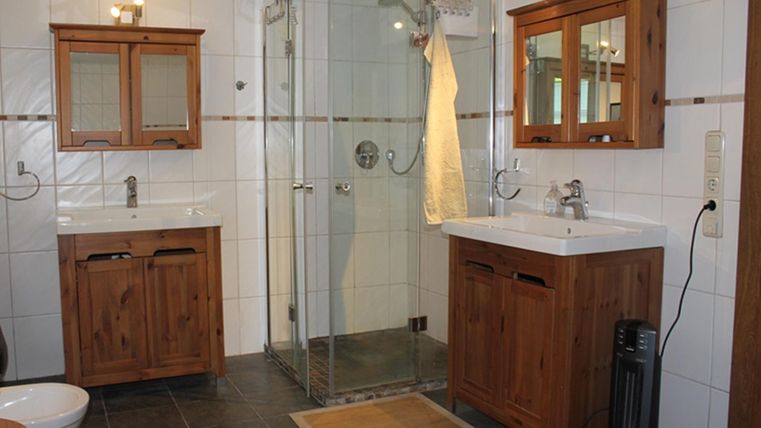 A modern bathroom with wooden cabinets and a shower cubicle. The floor is tiled with dark tiles and a rug adds extra comfort.