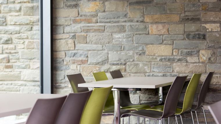 A modern interior with a table and colorful chairs. The wall is made of natural stone and creates a pleasant atmosphere.