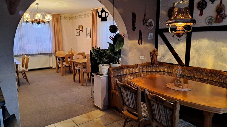 Een gezellige eetruimte met houten stoelen en een ronde tafel. Op de achtergrond zijn er extra zitplaatsen en aangenaam licht te zien.