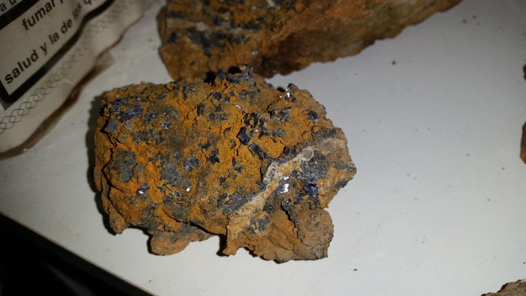 Ein Stück Gestein mit orangefarbener Oberfläche und kleinen glitzernden Mineralien. Die Struktur ist rau und unregelmäßig.