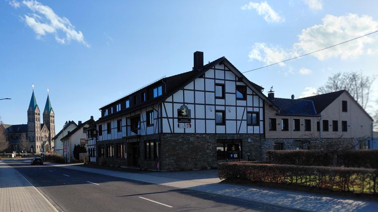 A charming half-timbered house with a street café. In the background, two pointed church towers are visible.