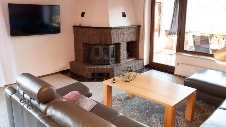 A modern living room with a cozy fireplace and a large television. The furniture is simple and inviting, complemented by a wooden table and a carpet.
