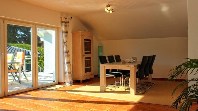 Een lichte eetkamer met een grote tafel en zwarte stoelen. Grote ramen laten veel licht binnen en bieden uitzicht op het terras.