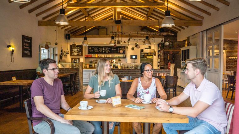 A group of four friends sits at a wooden table in a cozy café. They laugh and enjoy their drinks in an inviting atmosphere.