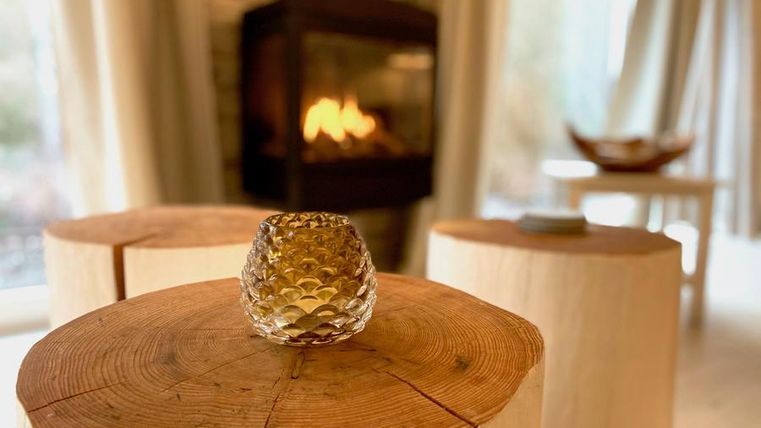 Ein gemütlicher Raum mit einem warmen Kamin und Holzstühlen. Auf einem Tisch steht ein dekoratives Glasobjekt.