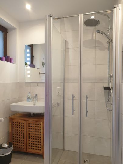 A modern shower with glass doors and a rainfall showerhead. The room features bright tiles and a stylish sink setup.