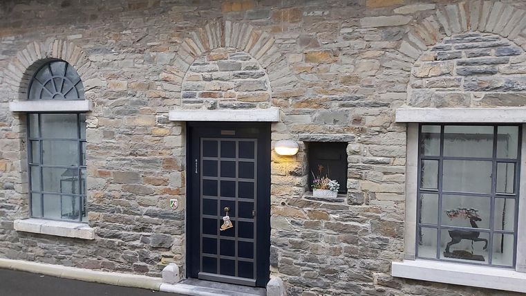 A historical stone wall with windows and a black door. The facade appears rustic and inviting.