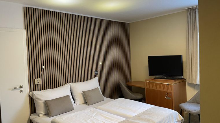 Een moderne hotelkamer met een tweepersoonsbed en een comfortabele zitgelegenheid. Aan de muur hangt een televisie, en de inrichting is eenvoudig en elegant.