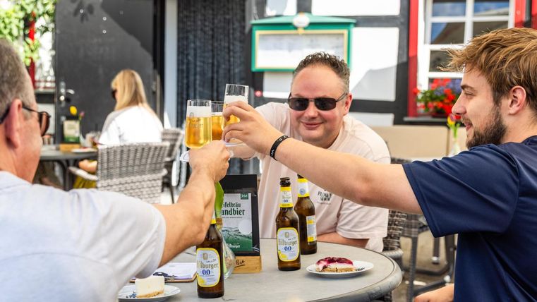 A cheerful group of friends toasting with a beer. In the background, chairs and tables can be seen in an inviting beer garden.