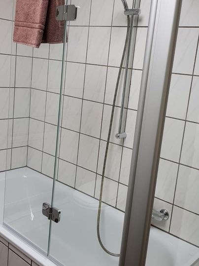 Een moderne badkamer met een bad en een glazen douchewand. Een roze handdoek hangt aan de muur.
