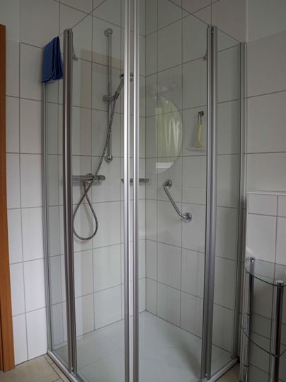 A modern shower with crystal-clear walls and silver frames. The walls are tiled and the fittings are functional.