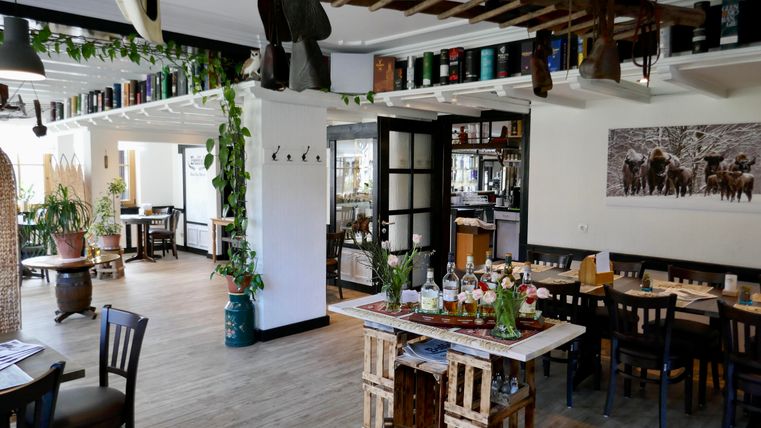 A modern restaurant with wood and plant accents. The decor is cozy and inviting, featuring tables and decorative elements.
