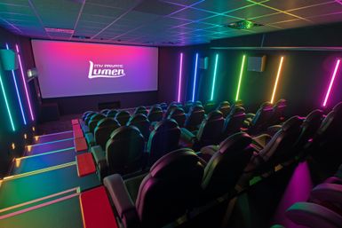 Ein modernes Kino mit bequemen Sitzen und bunten Lichtern. Die Leinwand zeigt das Logo von "Lumen".