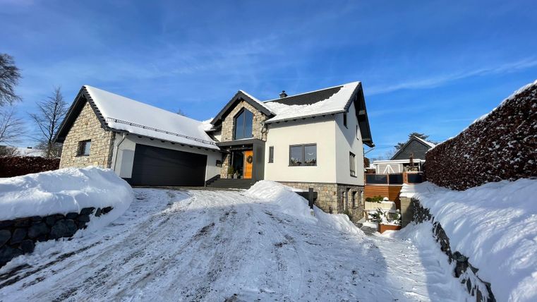 A modern house with a snow-covered front yard. The sky is clear and blue.