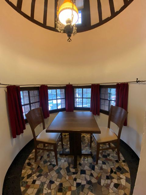 Een gezellige ronde kamer met twee stoelen en een tafel. De ramen zijn omringd door rode gordijnen en de vloer heeft een interessant patroon.