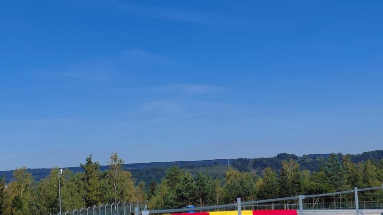 A racetrack with a clear blue sky. In the background, there are trees and the surrounding landscape.