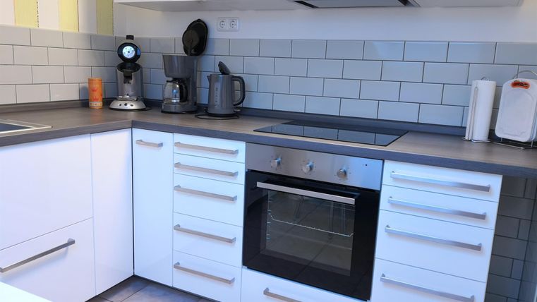 Een moderne keuken met witte kasten en grijze werkbladen. Op het aanrecht staan verschillende keukenapparaten zoals een waterkoker en een koffiezetapparaat.