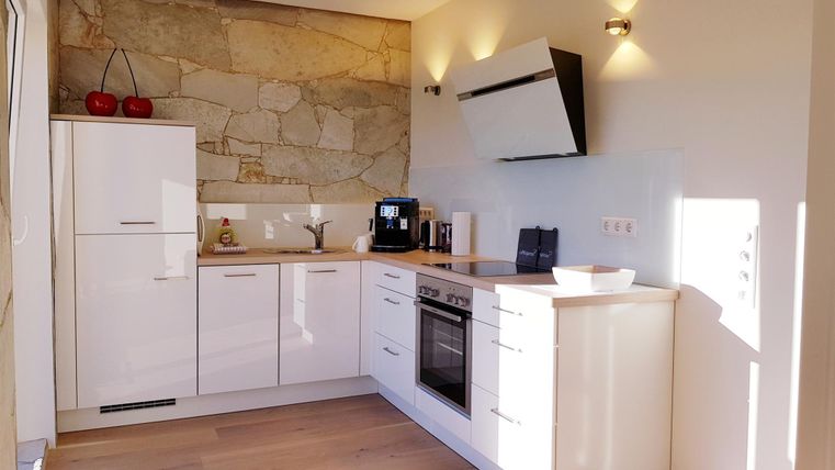 A modern kitchen with white furniture and bright walls. The large windows provide plenty of natural light.