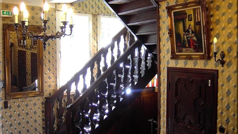 Eine elegante Treppe aus Holz führt in den oberen Stock. Die Wände sind mit einem klassischen Muster und einigen Gemälden dekoriert.