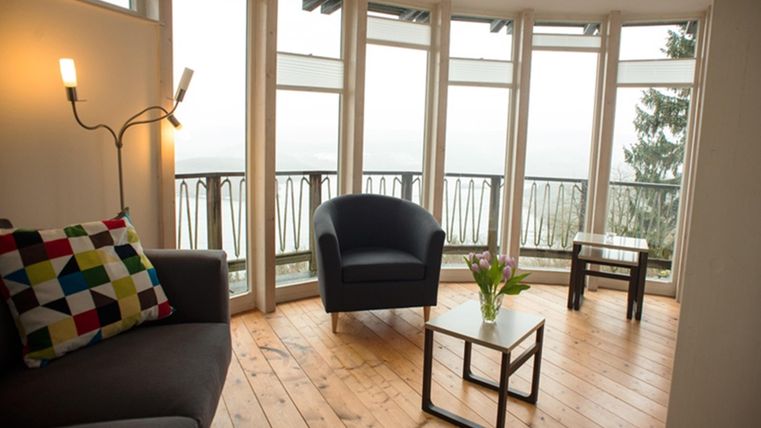 A cozy room with large windows and a view of the landscape. There is a sofa area with colorful pillows and a small table with fresh flowers.