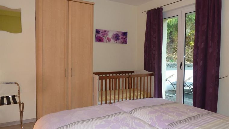 A cozy bedroom with a double bed and a crib. Large windows lead to a balcony and the walls are painted in soft colors.