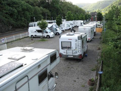 Ein Stellplatz für Wohnmobile mit mehreren Fahrzeugen. Umgeben von Bäumen und sanften Hügeln.