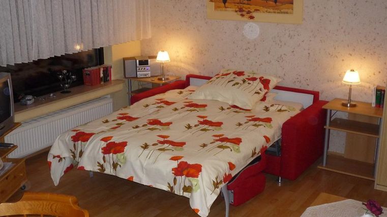 Ein gemütliches Schlafzimmer mit einem roten Sofa-Bett und einer blumigen Bettdecke. Sanftes Licht von den Nachttischlampen schafft eine einladende Atmosphäre.