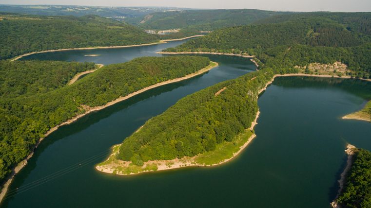 A picturesque landscape with a winding river and forested banks. The green surroundings and clear water invite relaxation.