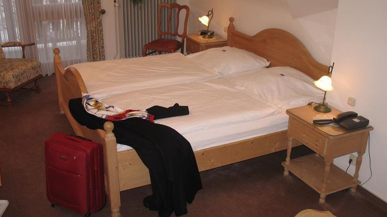 A cozy hotel room with two beds and a red suitcase. There is a table, a chair, and a lamp that create an inviting atmosphere.