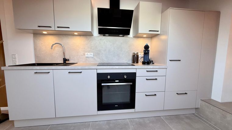 Een moderne keuken met grijze kasten en een kookplaat. Het werkblad is van steen en er is een elegante afzuigkap.
