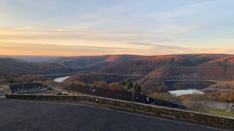 A picturesque landscape with gentle hills and tranquil waters. The sky shines in warm colors of the sunset.