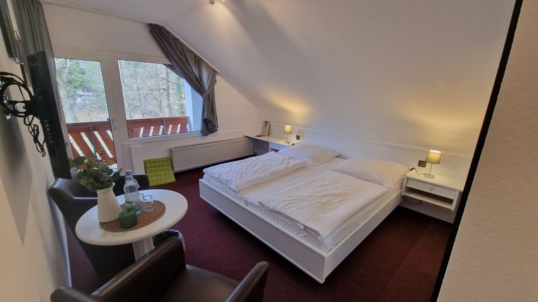 A cozy room with a double bed and two armchairs. Large windows provide plenty of light and a view outside.